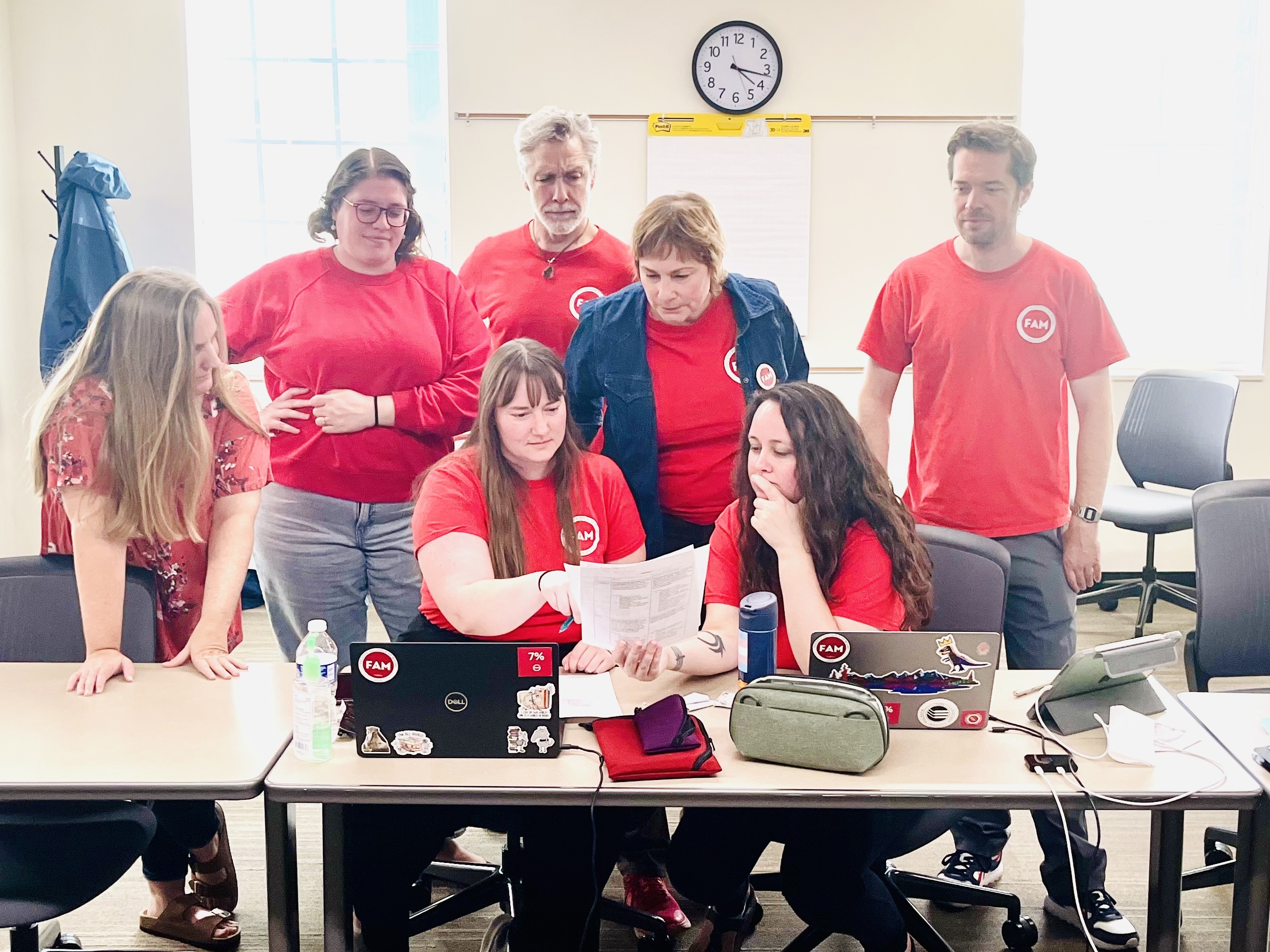 FAM NT in red shirts, surrounding a laptop and examining a document