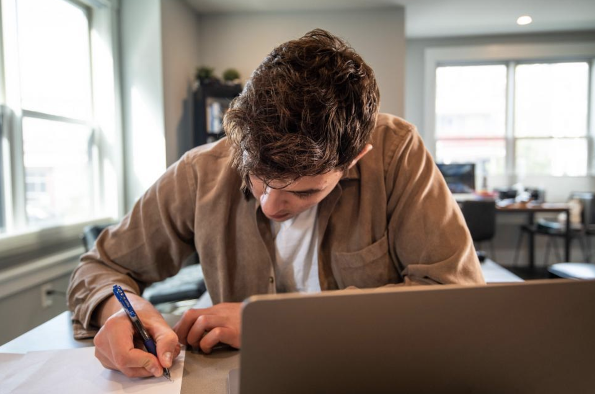 An individual writes while multitasking at a home office