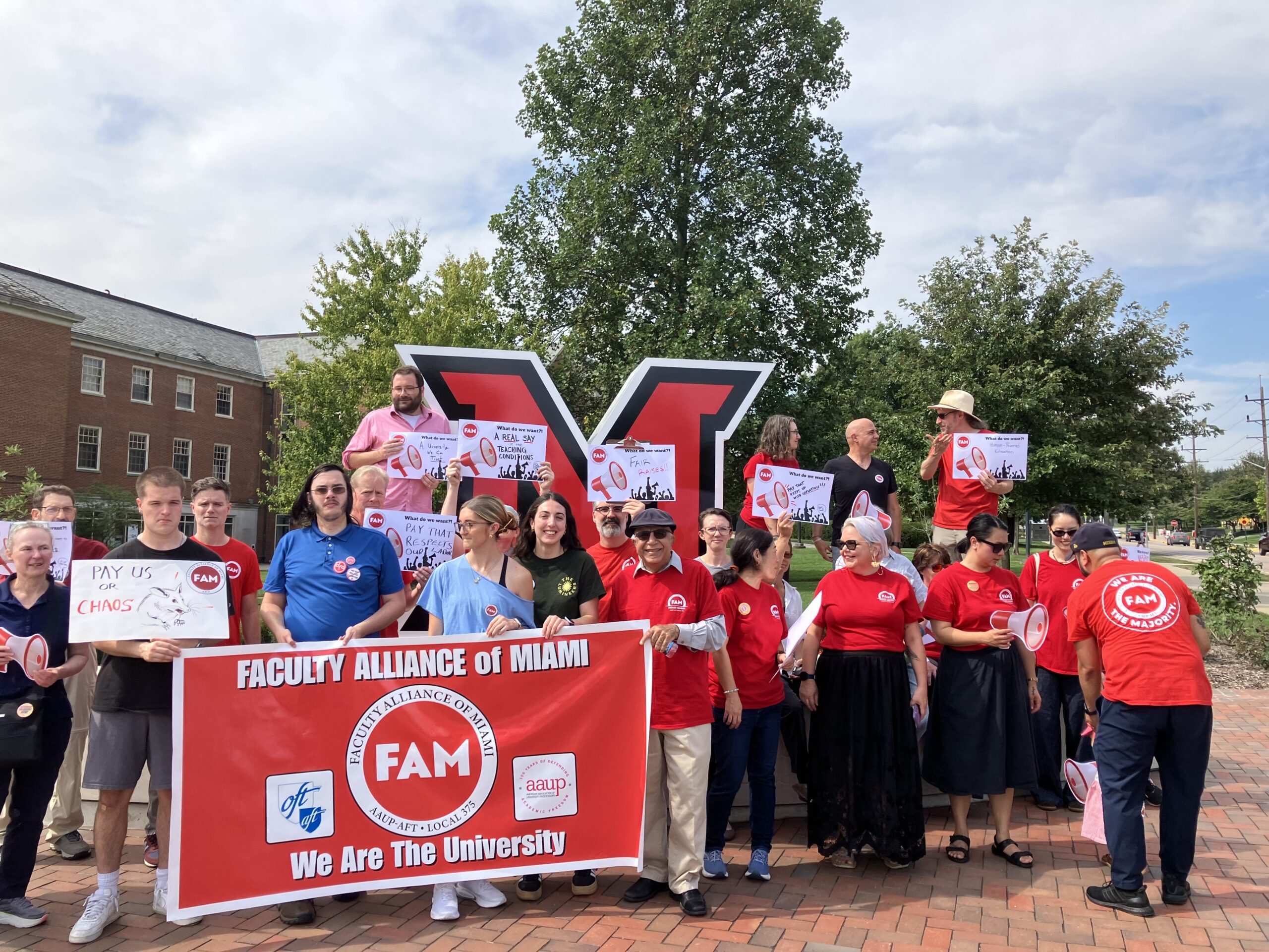 Students, librarians, and faculty in FAM tees show signs in support of fair raises by the giant Miami M